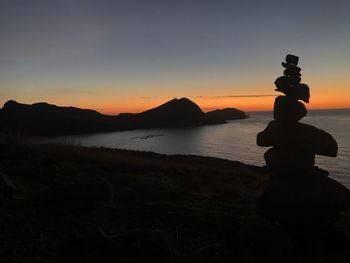 Silhouette rocks on beach against sky during sunset