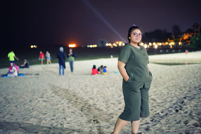 Portrait of mid adult woman standing on beach against sky at night