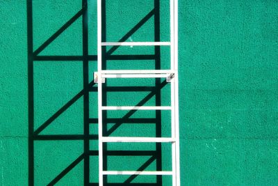 Close-up of metal ladder against green stucco wall