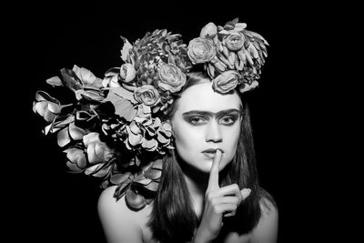 Portrait of fashion model wearing flowers with finger on lips against black background