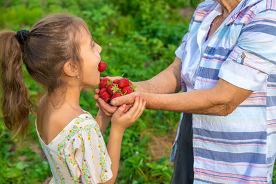 Smiling girl eating strawberry standing in front of grandmother