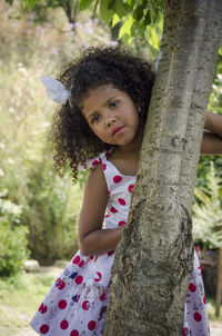 Portrait of girl standing by tree trunk