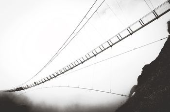 Low angle view of people walking on cable bridge in foggy weather