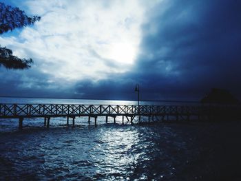 Silhouette pier over sea against cloudy sky
