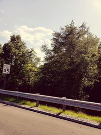 Empty road by trees against sky in city