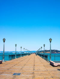 Walkway by sea against clear blue sky