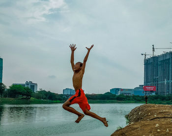 Full length of shirtless man jumping in city against sky