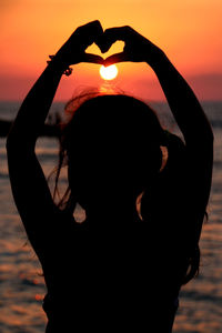 Rear view of silhouette woman standing against sea during sunset