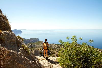 Rear view of woman on mountain by sea against clear sky