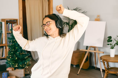 Portrait of young woman with arms raised standing at home