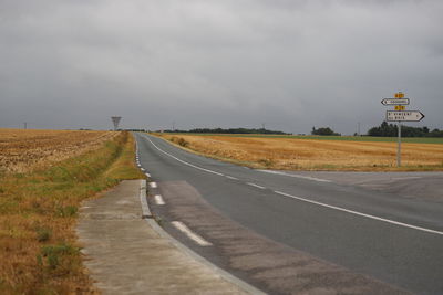 Road amidst cut cornfields against moody sky with water tower, saint vincent des bois, france