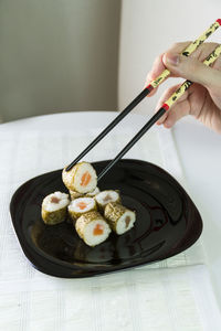 Cropped image of hand holding sushi with chopsticks