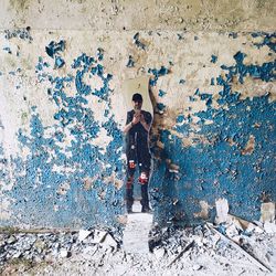 Full length of man photographing while reflecting on mirror against weathered wall