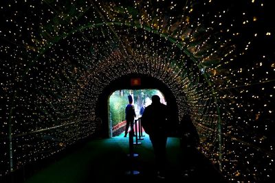 Rear view of people standing in illuminated tunnel