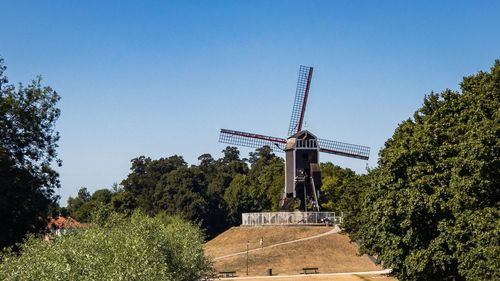 Traditional windmill against clear blue sky on hill with trees