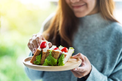 Closeup image of a woman holding and eating whole wheat sandwich in wooden plate