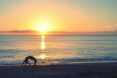 Silhouette woman exercising at beach during sunset