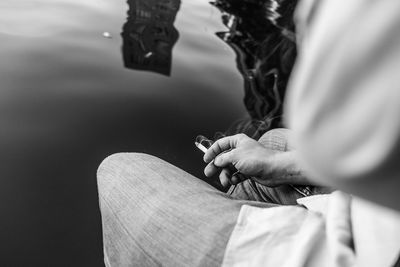 Midsection of man holding burning cigarette by lake