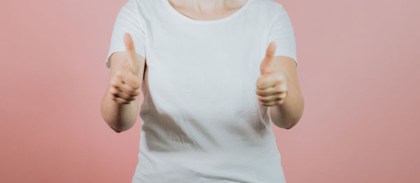 Midsection of woman gesturing while standing against pink background