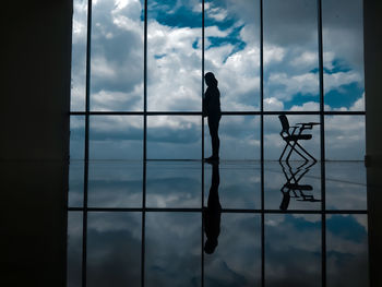 Silhouette man standing by window against sky