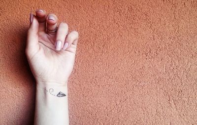 Cropped image of hand with tattoo against brown wall