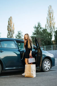 Shopping, sale, happy young stylish blonde woman with shopping bags opening car after shopping. 