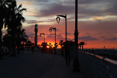 Street lights by silhouette trees against sky during sunset