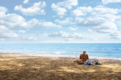 Rear view of man sitting on beach against sky