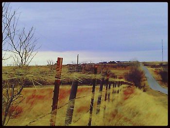 Fence on field against cloudy sky
