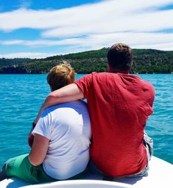 Rear view of father with son sitting on boat against cloudy sky during sunny day