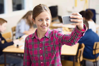 Smiling schoolgirl taking self-portrait in classroom