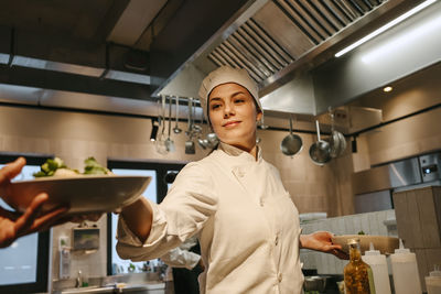 Female chef passing salad bowl to colleague working in illuminated kitchen
