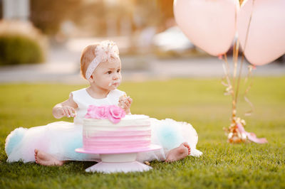 Baby girl 1 year old wear princess dress eating birthday cream cheese cake sitting on grass