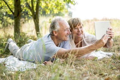 Happy senior couple lying in meadow takinhg a selfie with tablet