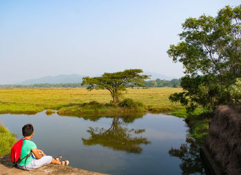 Rear view of man sitting on field against sky