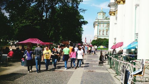 People on sidewalk in city against sky