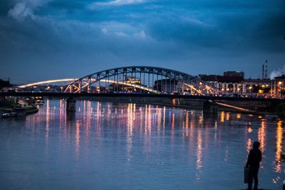 Illuminated bridge over calm river against sky