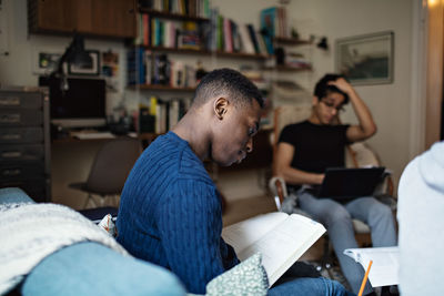 Studious male friends doing homework while sitting in living room