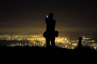 Person photographing illuminated cityscape at night