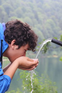 Young man drinking water from hose against lake