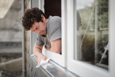Caucasian man cleans window frames outside.