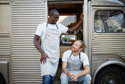 Smiling male owners looking at each other outside food truck