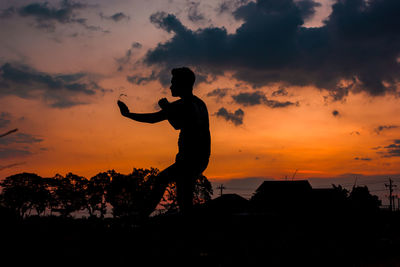 Silhouette woman standing on field against sky during sunset