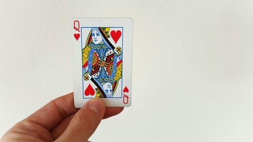 Cropped image of hand holding queen of hearts against white wall