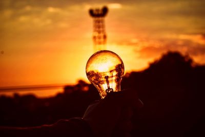 Close-up of silhouette hand holding light bulb during sunset