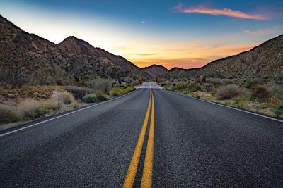 Empty road leading towards mountains against sky during sunset