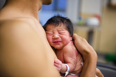 A newborn baby girl rests skin-to-skin against her father's chest