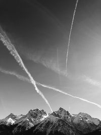 Low angle view of vapor trails over mountains against sky