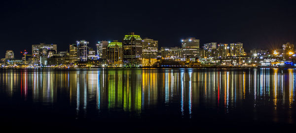 Illuminated buildings by river against sky at night