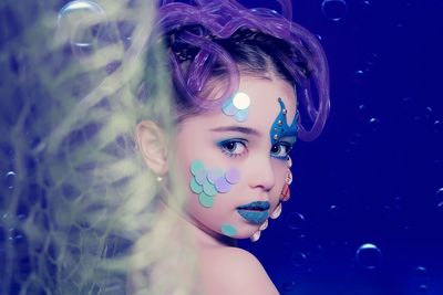 Close-up portrait of girl against blue backdrop